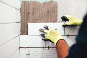 A man wearing yellow gloves is skillfully installing tiles on a wall.