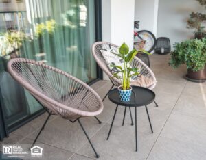 A stylish outdoor seating area with rattan chairs and a central table featuring a potted plant, set on a sleek tiled patio.
