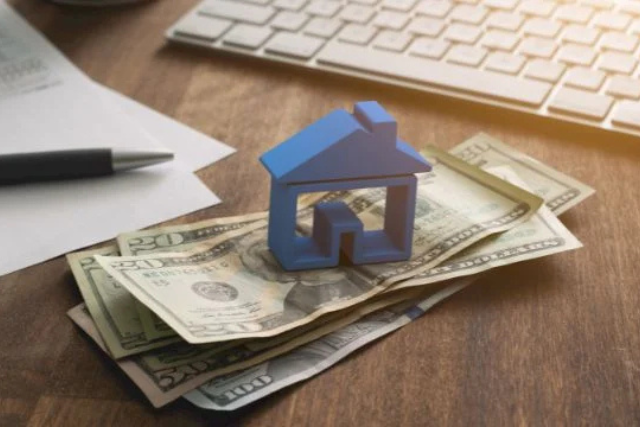 a-blue-home-figurine-resting-on-a-money-with-a-contract-in-the-background