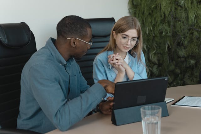 two-professionals-sitting-at-a-conference-table-discussing-information-displayed-on-a-tablet