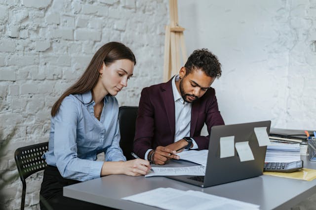 two-professionals-reviewing-documents-together-at-a-desk-with-a-laptop-and-office-supplies