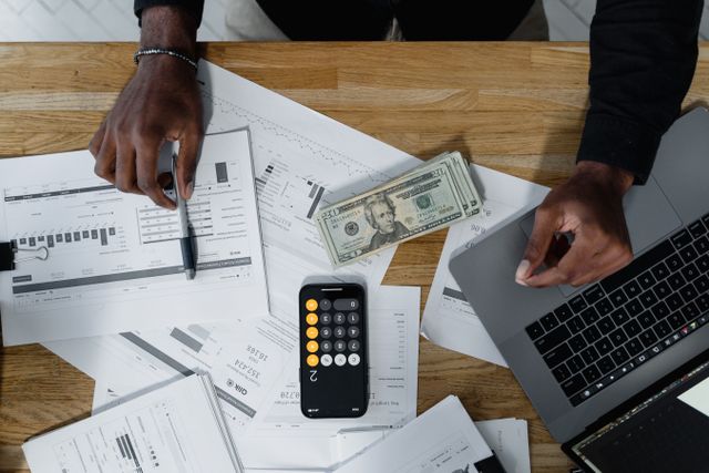 person calculating finances with documents and money on a desk