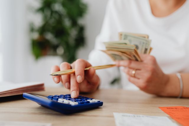 person using a calculator and holding money