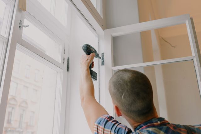 person fixing a window hinge with a drill