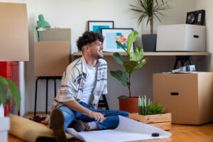 Young man moving into a new home, smiling while sitting amongst his things.