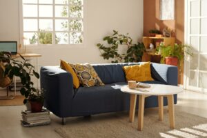 A modern living room featuring a blue couch with yellow pillows, a coffee table, and a cozy carpet.