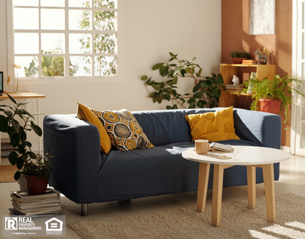 A modern living room featuring a blue couch with yellow pillows, a coffee table, and a cozy carpet.