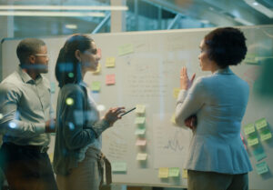 Real estate professionals discussing risk management strategies around a whiteboard filled with sticky notes.

