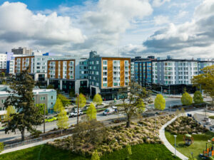 Multi-family housing view from above, park is in the foreground with white fluffy clouds.
