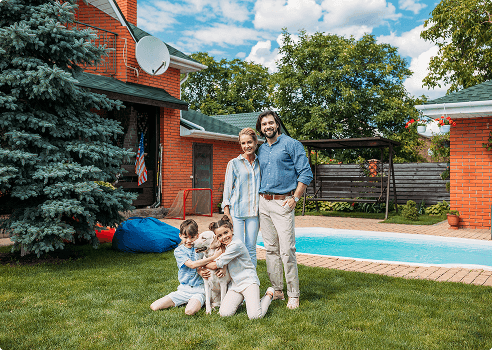 A family smiling with their two kids and dog, in front of a pool.