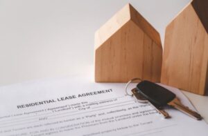 Close-up of rental agreement with house keys and wooden home models on a desk.