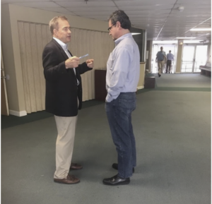 Two men speaking face to face in an indoor hallway.