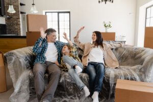 1 / 1 – A cheerful family sitting on a couch amidst moving boxes, celebrating their new home.jpg