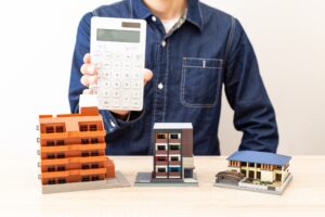 Man holding a calculator in front of a house model.