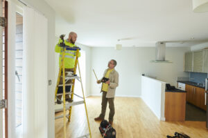 Two individuals in a rental property discussing maintenance, one on a ladder, the other carrying a tablet.