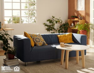 A modern living room featuring a blue couch with yellow pillows, a coffee table, and a cozy carpet.