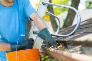 A man wearing a blue shirt and gloves diligently cleaning out a gutter, ensuring proper drainage.