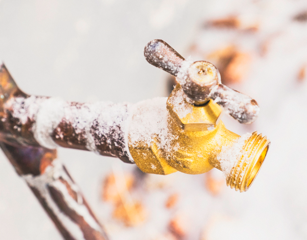 Frozen Outdoor Water Faucet and Pipes Covered in Snowflakes