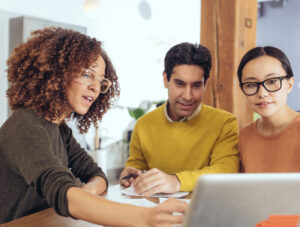 A real estate professional and two clients focus on a laptop.
