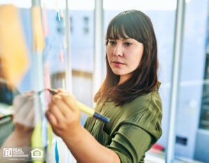 Property manager writing notes on a glass wall in an office, strategizing maintenance efforts.