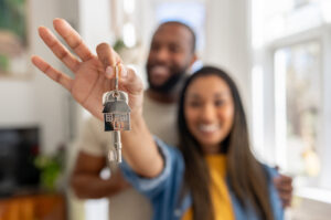 A smiling couple holds up keys to their new home.
