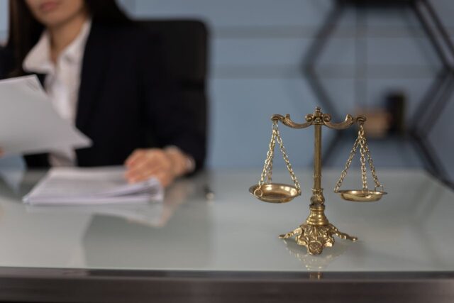 legal-scales-in-foreground-person-looking-at-papers-in-background legal scales and person writing