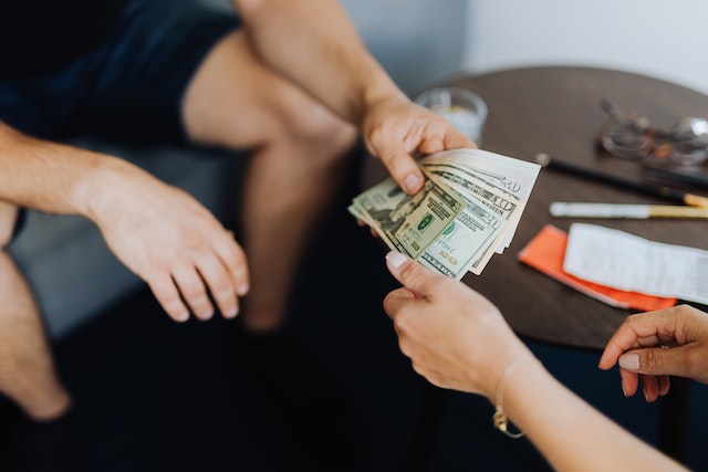 two-people-exchanging-cash-while-sitting-near-a-small-table