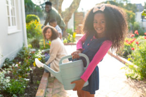 Happy african american girl and her family gardening and watering plants together.