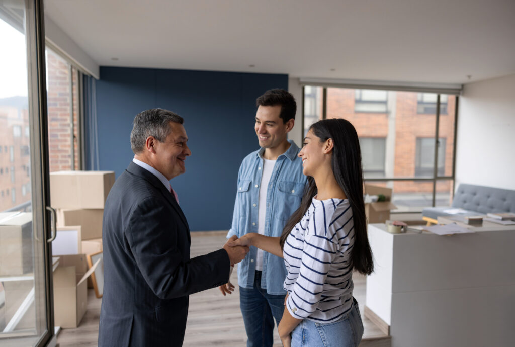 A couple in their new home, shaking hands with the propertymanager with smiles of satisfaction. 