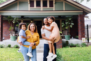 Portrait of parents holding their two kids in front of the house