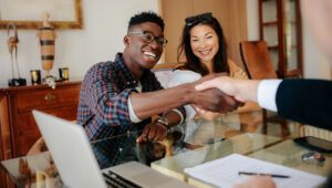 A couple at a table shaking hands with property manager, indicating the successful execution of a lease renewal.
