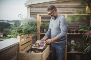 A man adds food scraps to a wooden compost box, promoting eco-friendly waste management.