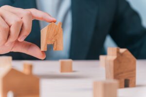 A person holds a wooden house model, symbolizing their real estate portfolio and investment in property.