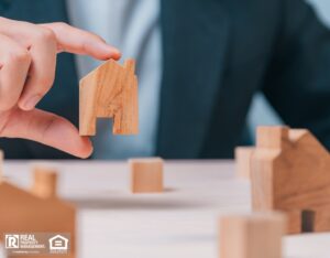 A person holds a wooden house model, symbolizing their real estate portfolio and investment in property.