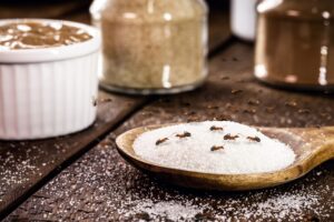 Close-up of ants on a pile of sugar and spices on a wooden surface.