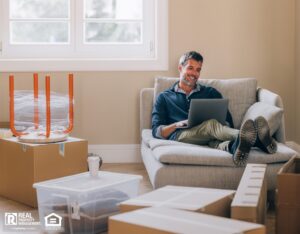 Man on his laptop in a room full of moving boxes.