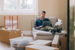 Man on his laptop in a room full of moving boxes.