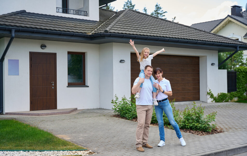 Smoke Rise Property Management Pleased caucasian mother and daughter on father's shoulders standing in front of new townhouse looking at camera outdoors in cloudy day. Family future planning, relationship and spending time together