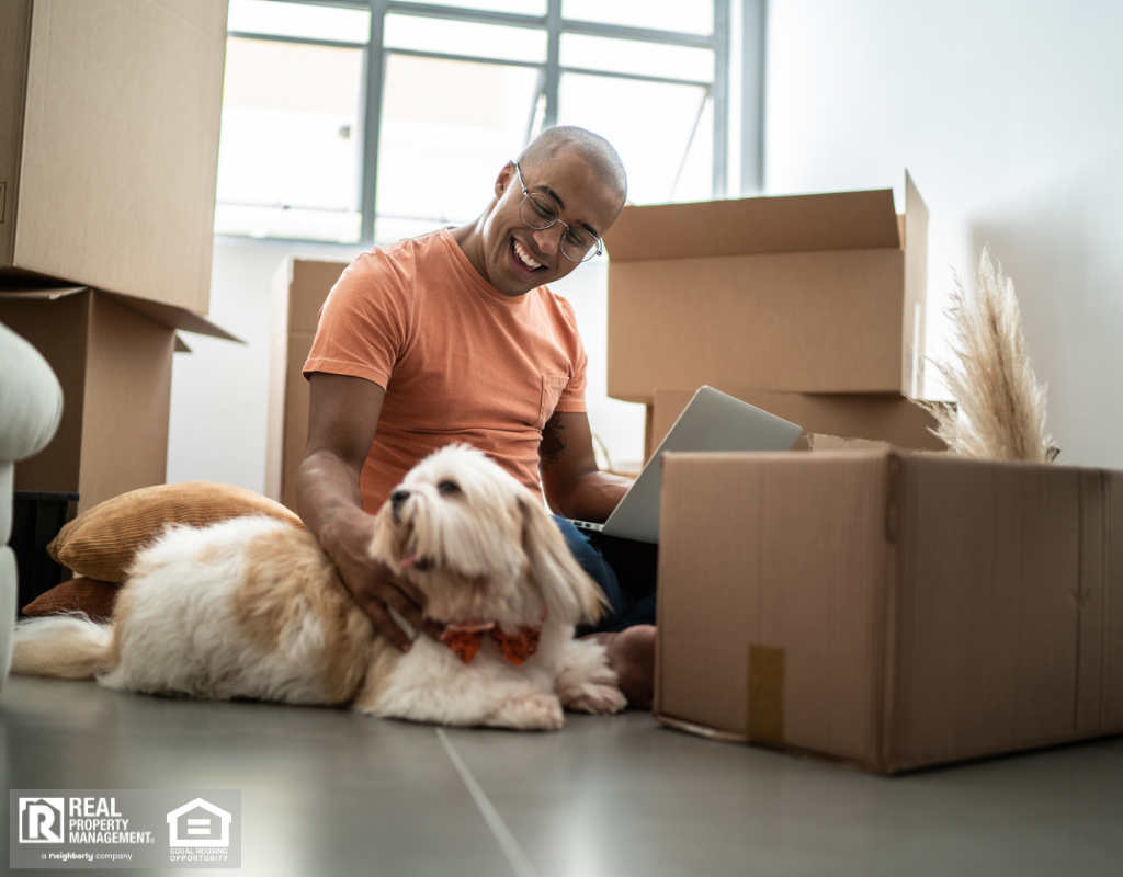 A man and his dog are seated on the floor, surrounded by boxes in their new home.