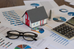 A house model, calculator, glasses, and property tax papers arranged on a desk. 