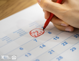 A woman's hand circles the "Pay Rent" date on her calendar.
