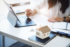 A woman uses a laptop with a house model on her desk, analyzing rental pricing strategies for rental properties. 