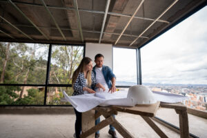A man and woman stand together in front of a home construction site, discussing the ongoing work.