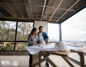 A man and woman stand together in front of a home construction site, discussing the ongoing work.