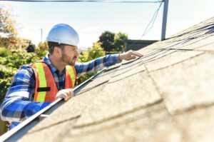Man with hard hat standing on ladder inspecting house roof.