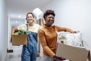 Two women actively moving boxes down a hallway, engaged in the process of relocating. 