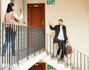 A man carrying a bag walks down the steps, waving goodbye to a female neighbor as they head to work.