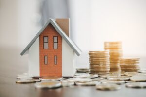 House model and money coin stacks on table, blurred background.