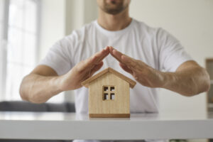 Close up of house model on table and man's hands above it, signifying home protection. 