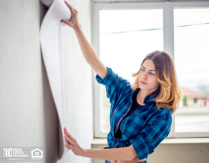 Woman choosing wallpaper and holding it up to the wall.
